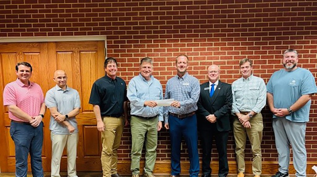 Men standing in a line with the two in the center holding a check for a donation