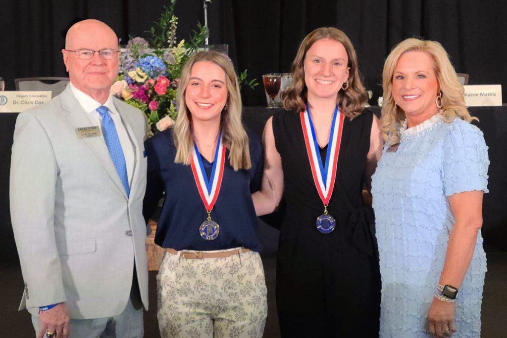 a man in a suit and his wife stand with two students wearing award medallions