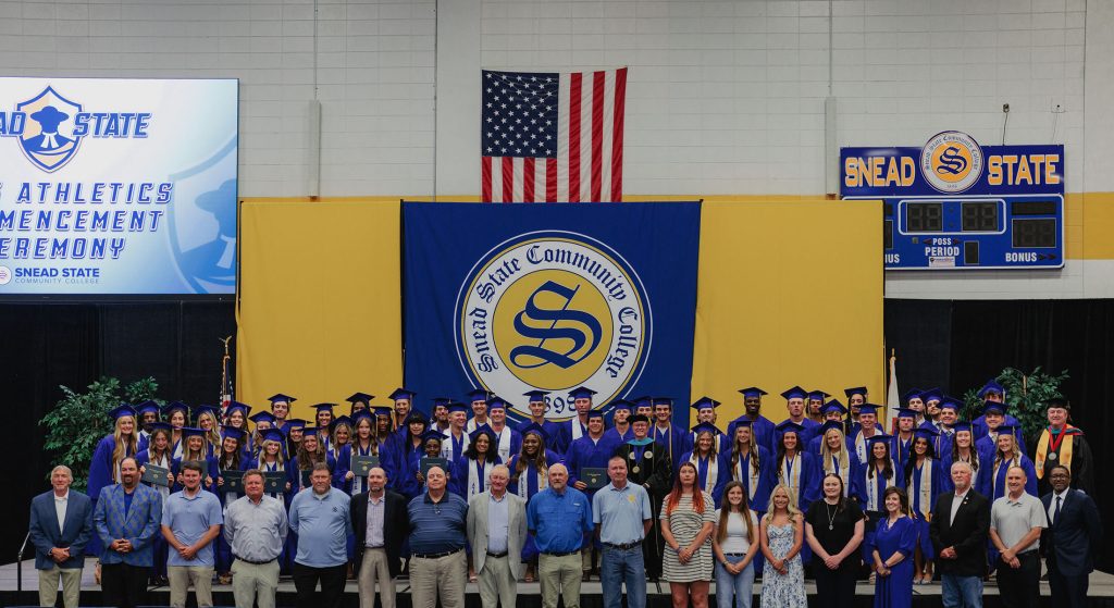 college athletes in their graduation caps and gowns standing with coaches and college administrators
