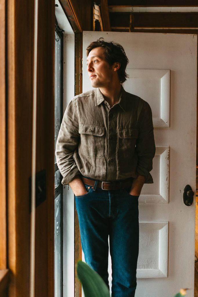 publicity shot of a musician standing in front of an open door looking out a window with his hands in his pockets