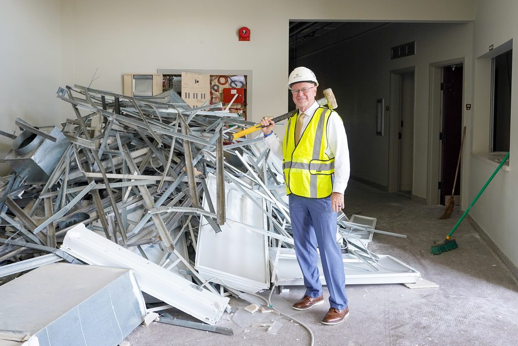 man wearing a hard hat and safety vest with a sledgehammer standing next to rubble inside a building renovation